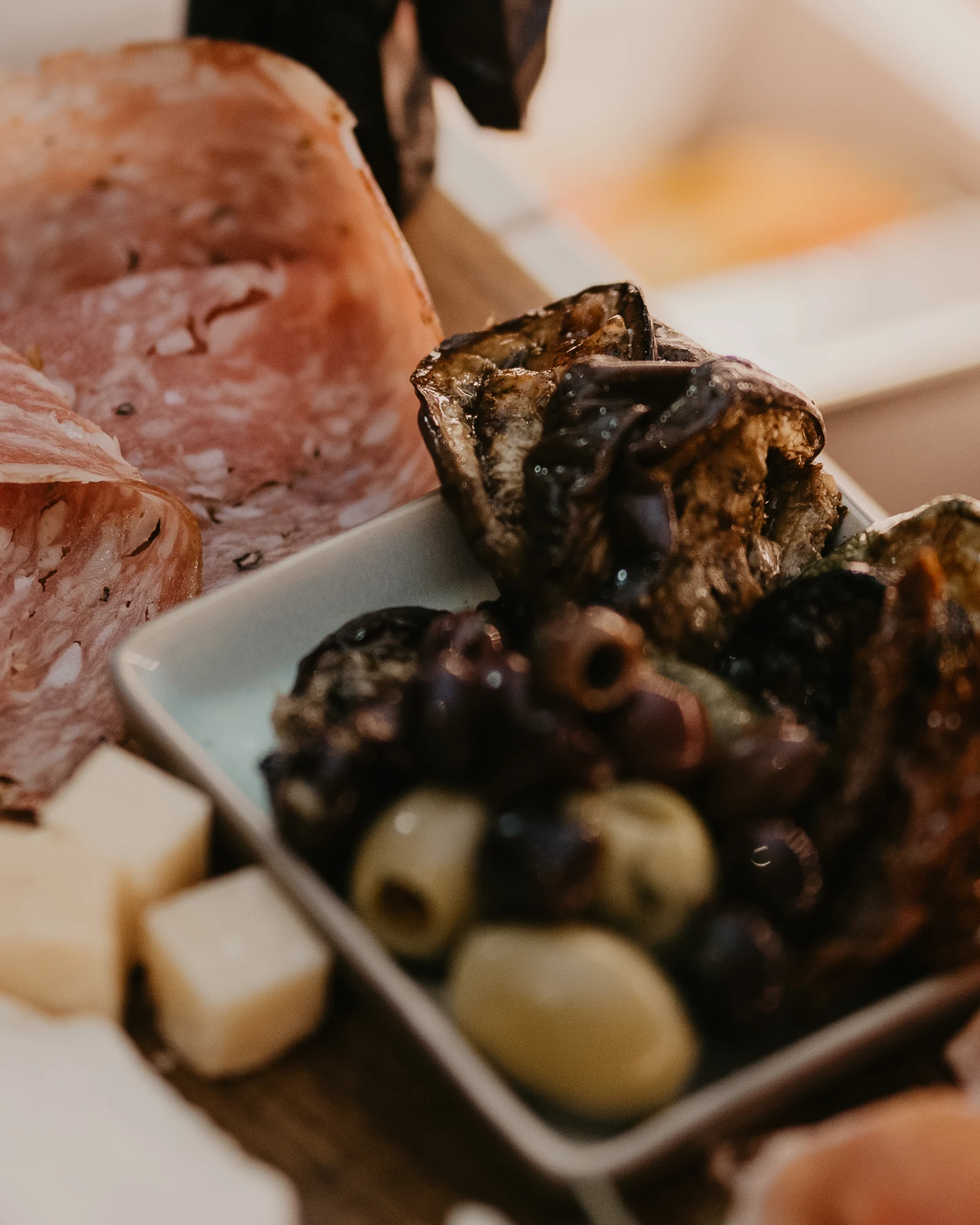Antipasti auf dem Holzbrett: Salami, Oliven, gegrilltes Gemüse, Käse und Schinken, angerichtet an der Feinkosttheke