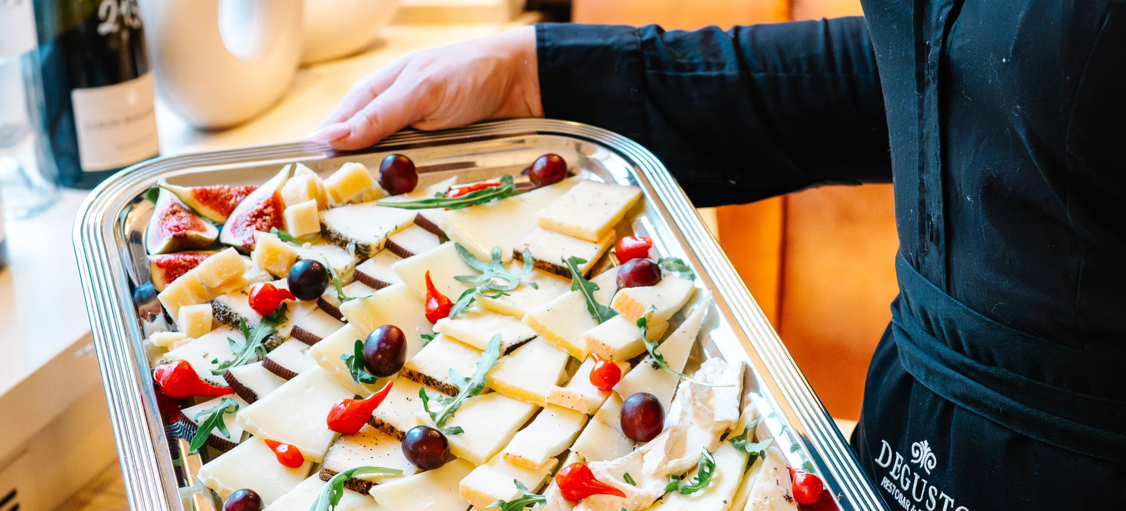 Eine DEGUSTO-Mitarbeiterin trägt ein Blech mit Käsevariation, Feigen und Trauben