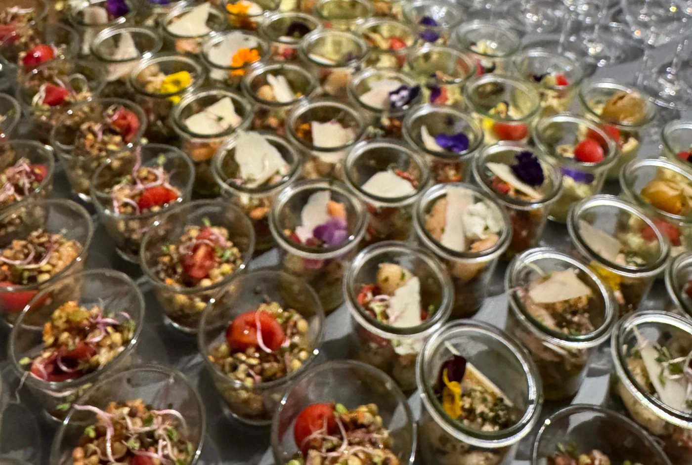 Viele Gläser mit Salaten, garniert mit essbaren Blüten und Parmesan
