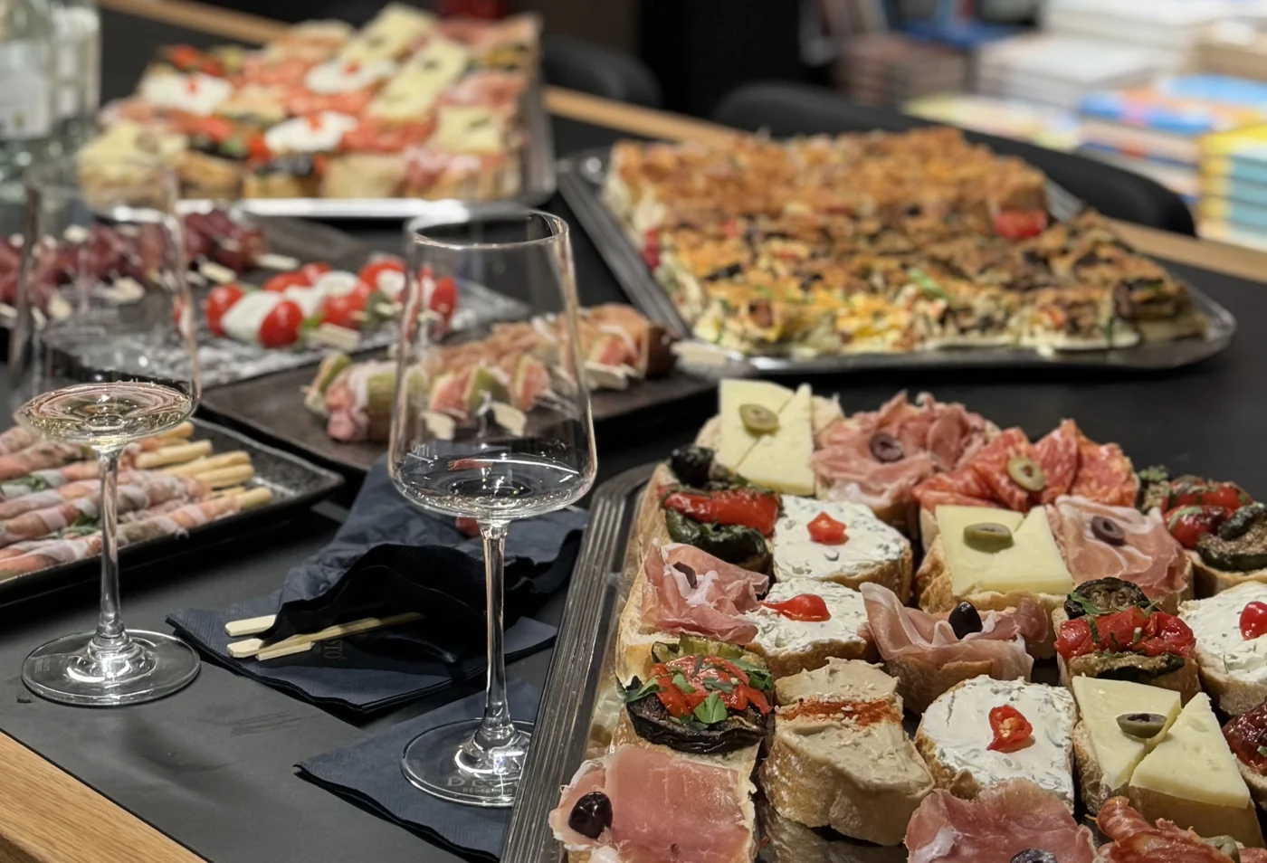 Eine lange Tafel mit Canapés, Spießen, Grissini und Quiche, daneben Weingläser und DEGUSTO-Servietten