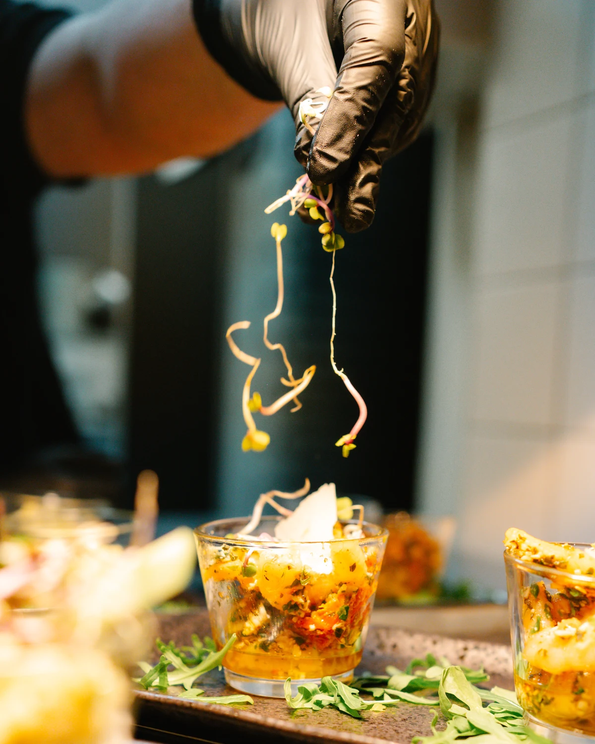 Eine Hand im Handschuh legt Sprossen auf ein Glas mit Salat