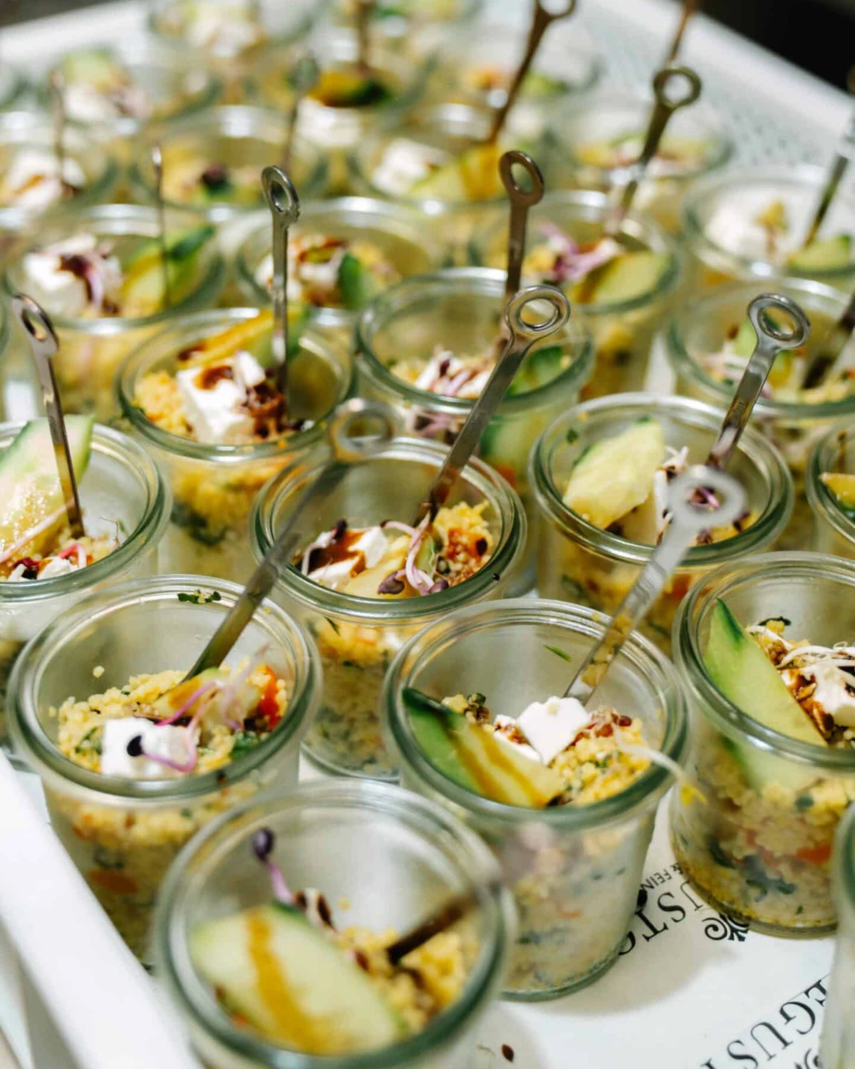 Gläser mit Couscous-Salat, Gemüse und Feta, in jedem ein Spieß, dicht an dicht in einer DEGUSTO-Kiste