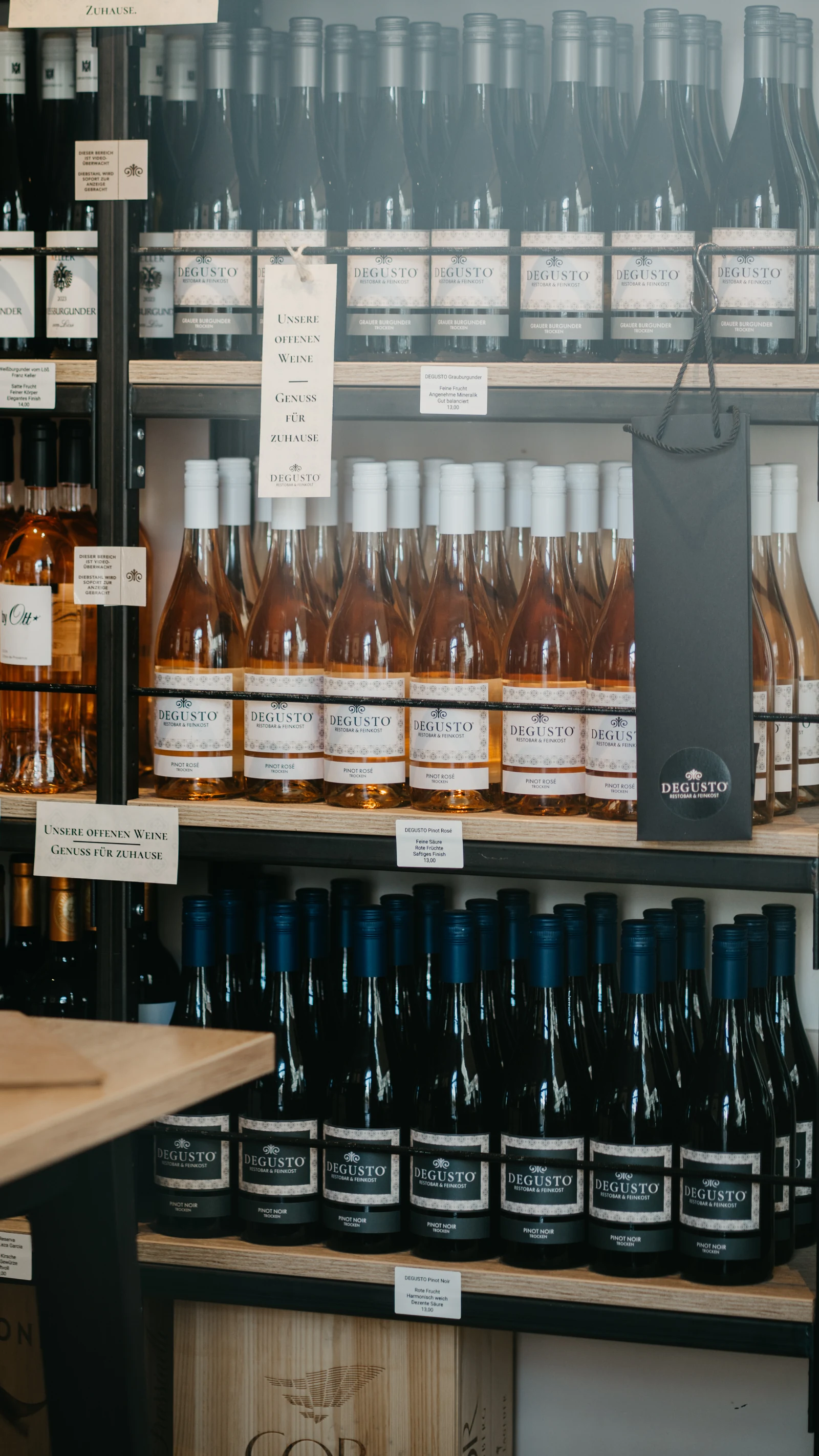 Regalreihen mit DEGUSTO Pinot Rosé und Pinot Noir unter eigenem Etikett, daneben eine DEGUSTO-Flaschentasche