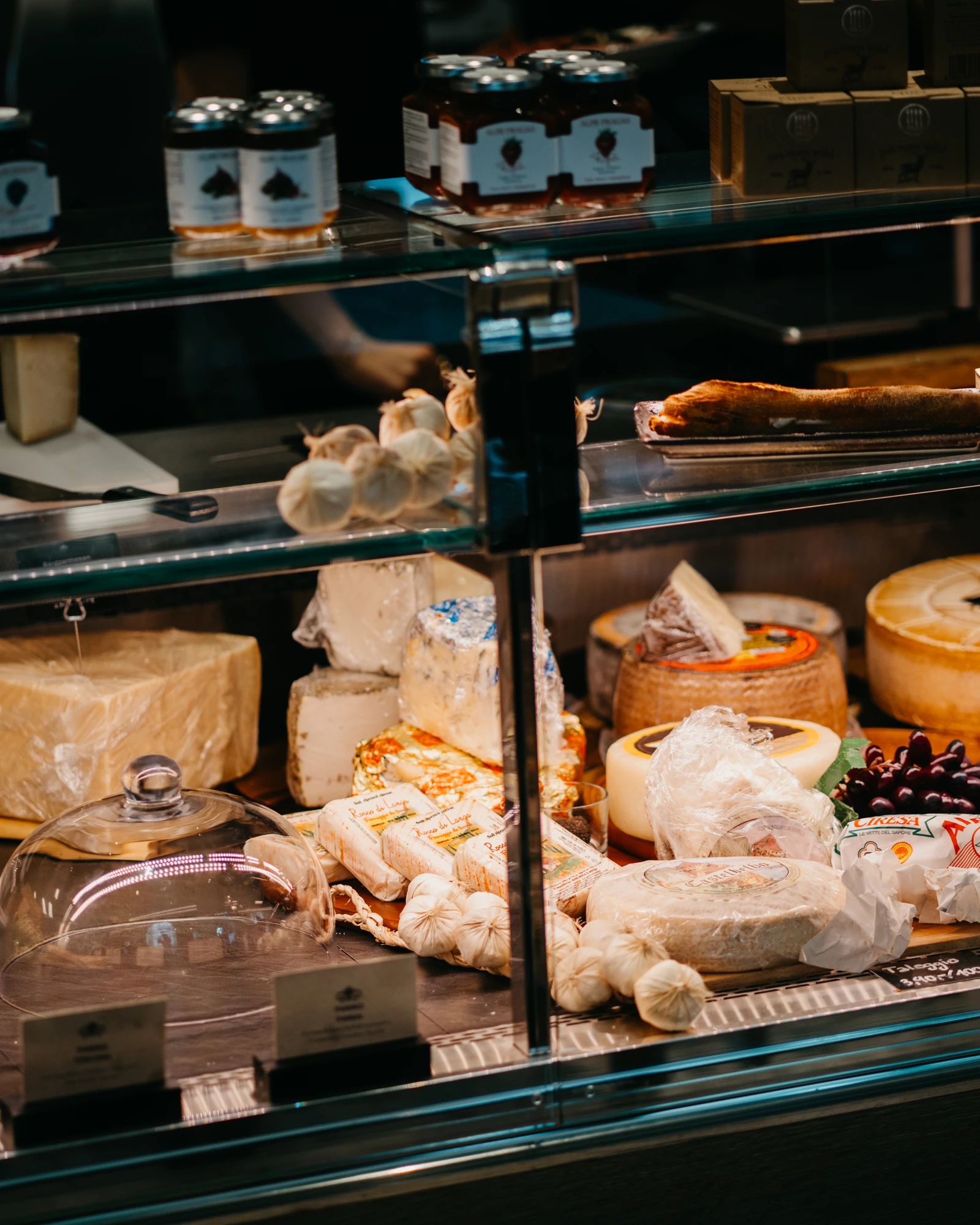 Blick in die gefüllte Feinkostvitrine mit Käse, Schinken und Parmesan, darüber das Regal