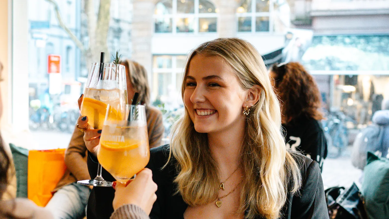 Zwei Gäste stoßen am Fensterplatz mit Spritz an, im Hintergrund die Freiburger Straße