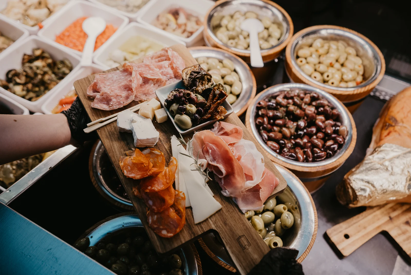 An der Feinkosttheke wird ein Holzbrett mit Salami, Schinken, Käse und Oliven aus den Schalen zusammengestellt