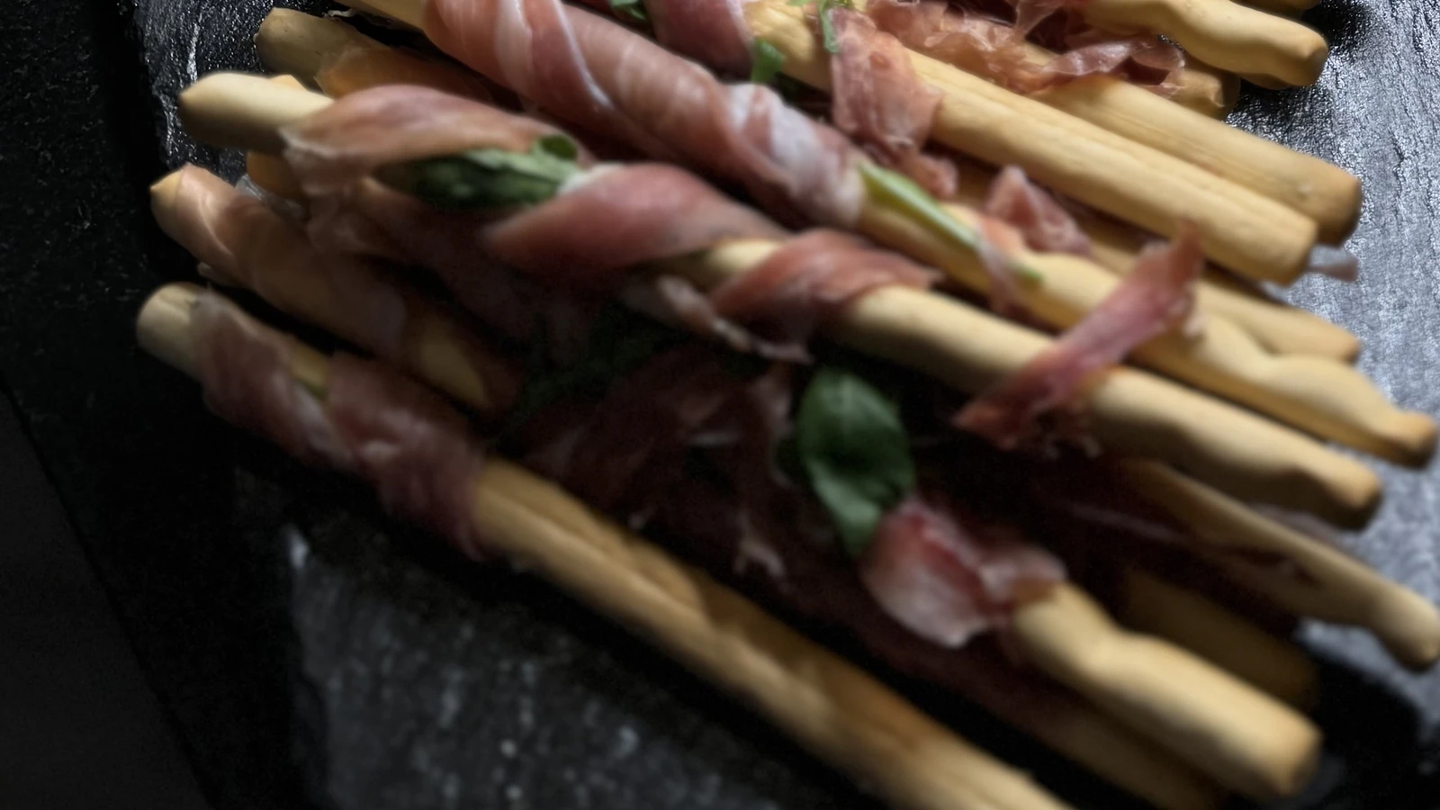 Mit Parmaschinken umwickelte Grissini auf einer Schieferplatte