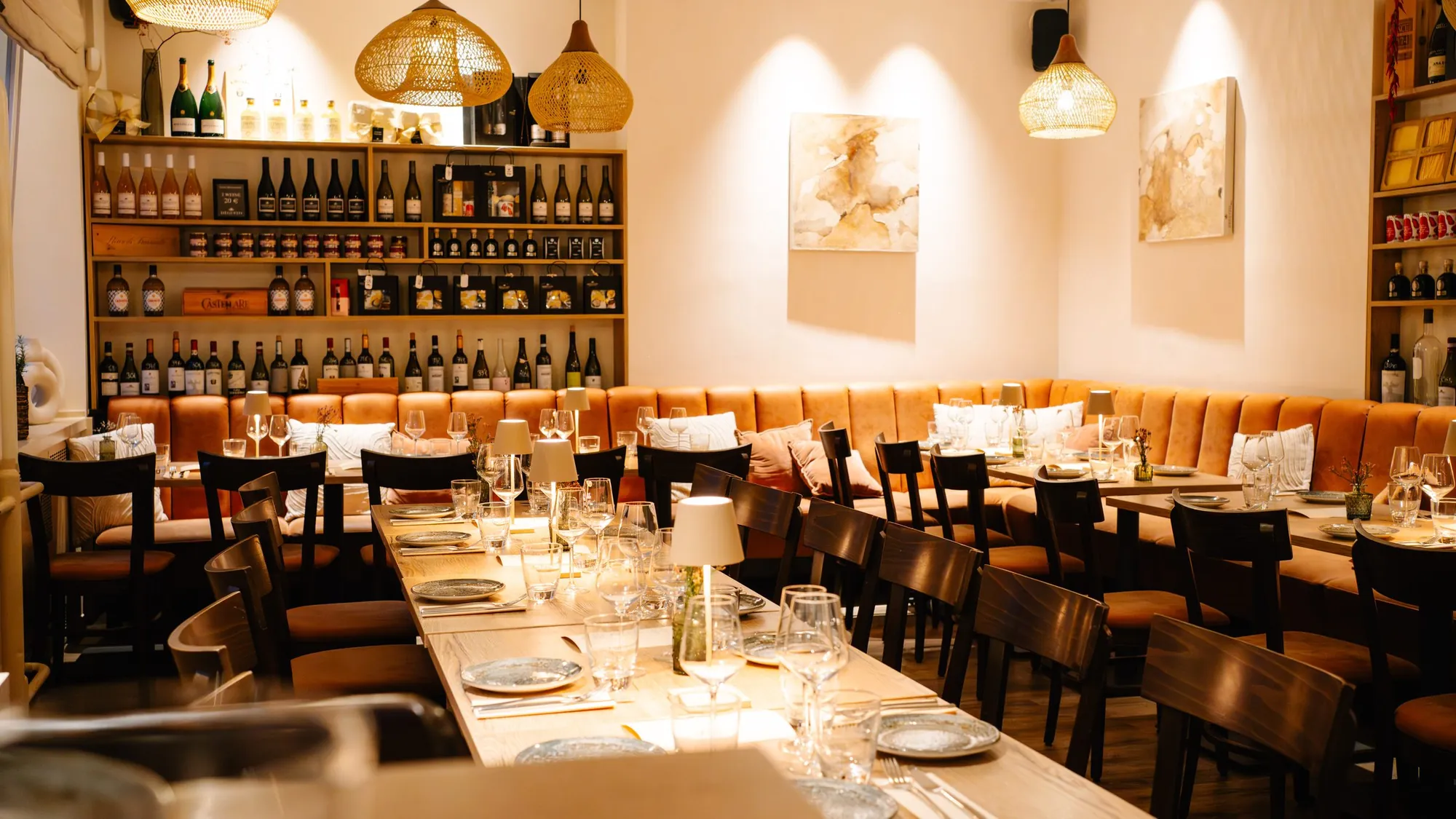 Der eingedeckte Gastraum von DEGUSTO mit Weinregal, Korblampen und Sitzbänken
