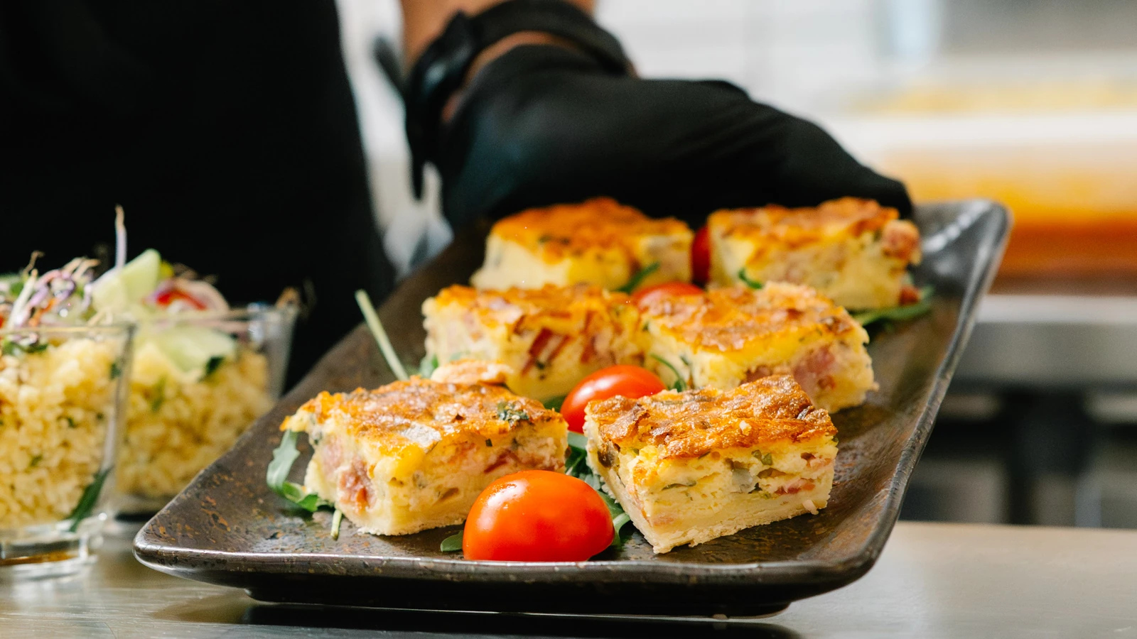 Quiche in Stücken auf einem Blech, daneben Salate im Glas