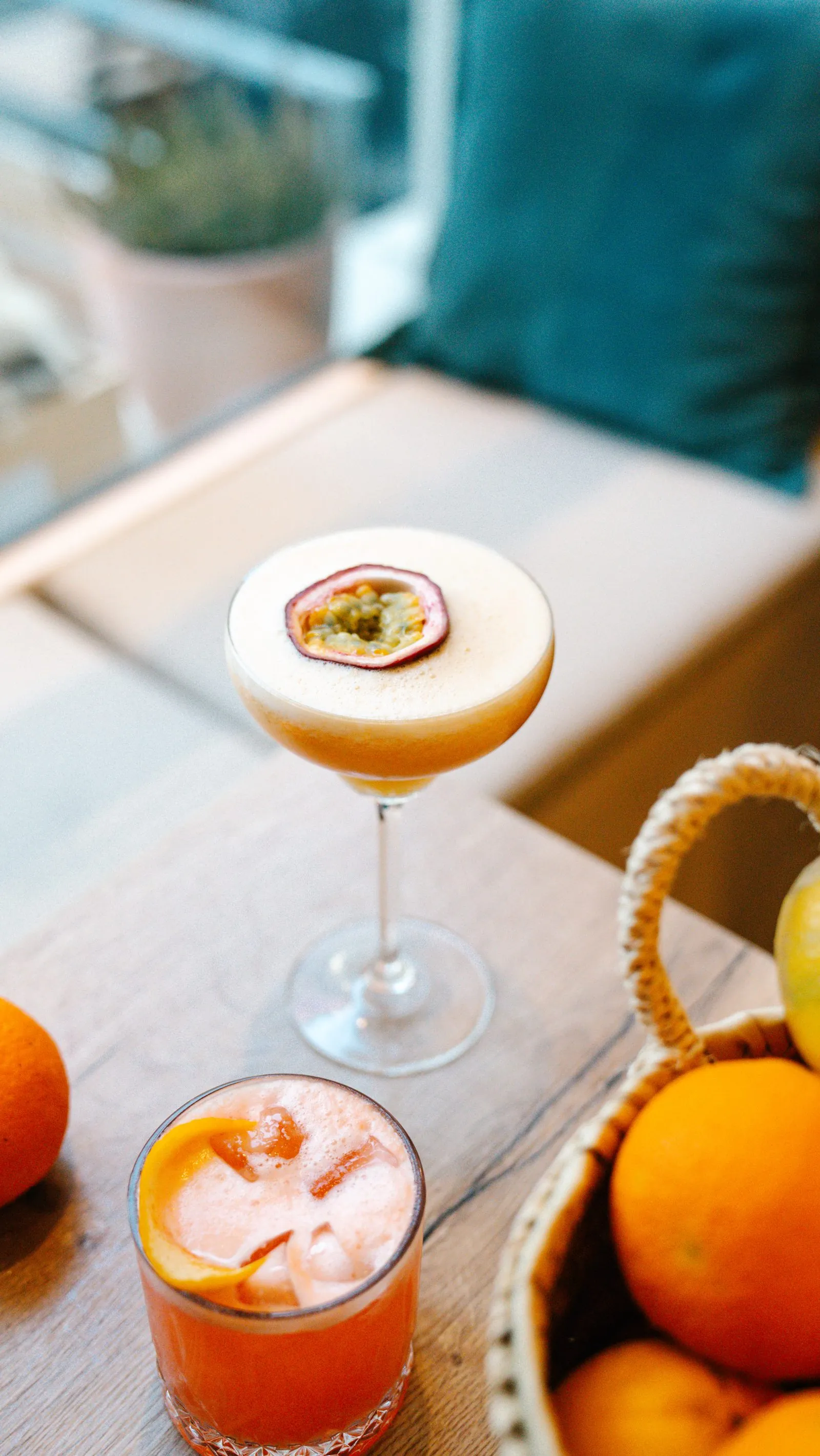 Zwei Cocktails am Fensterplatz der DEGUSTO Restobar, daneben ein Korb mit Orangen