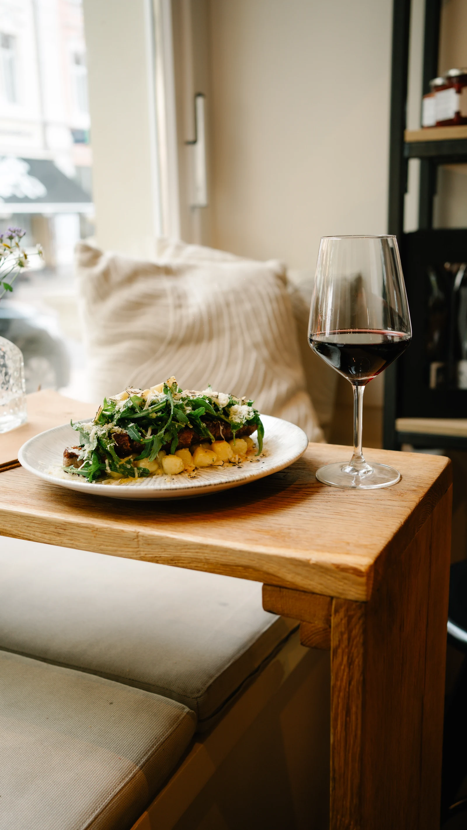 Tagliata mit Rucola und Parmesan auf einem Holztisch am Fenster, daneben ein Glas Rotwein