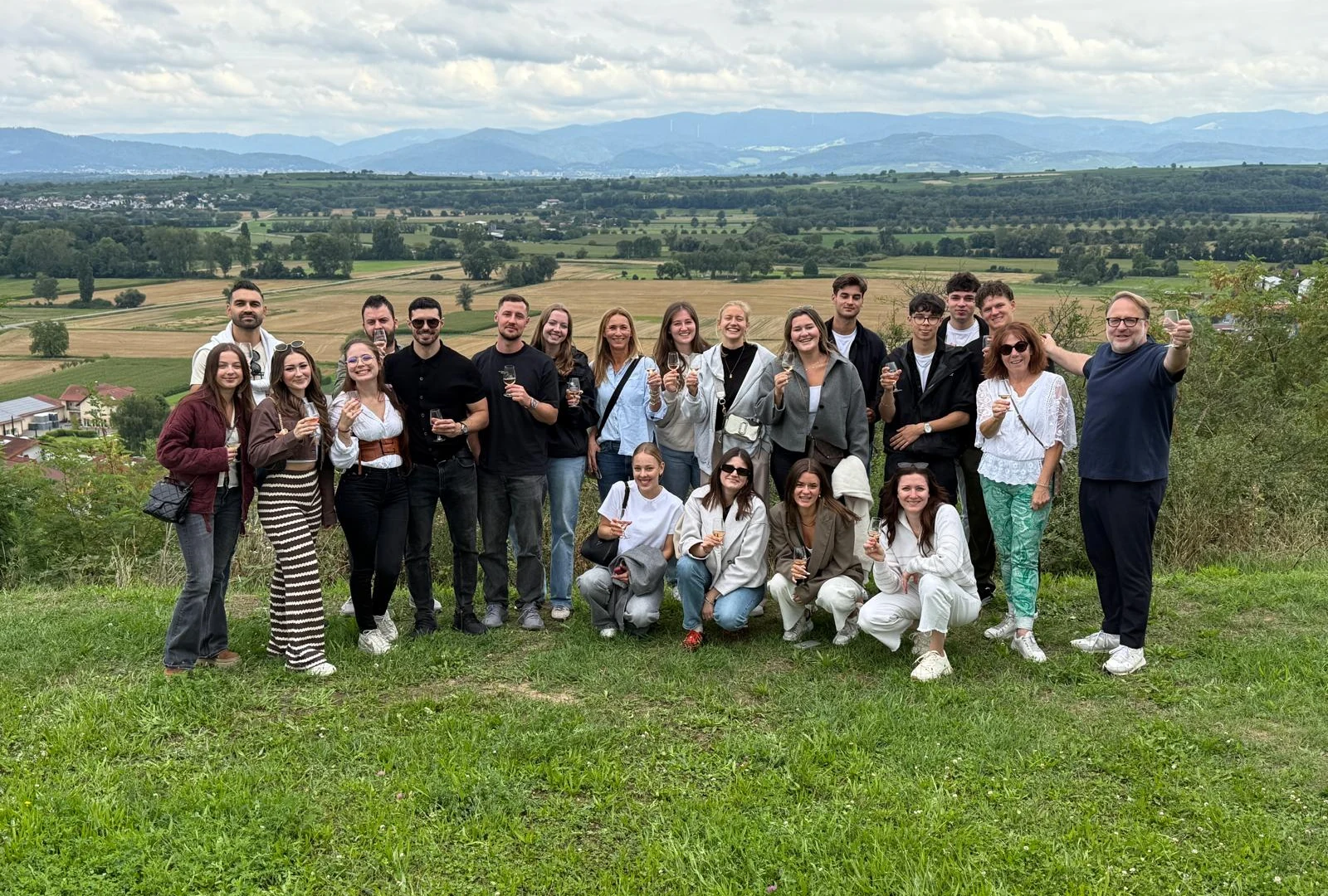Das DEGUSTO-Team auf einer Wiese über den Reben, rund zwanzig Personen nebeneinander, jede mit einem Glas in der Hand, dahinter die Rheinebene und der Schwarzwald