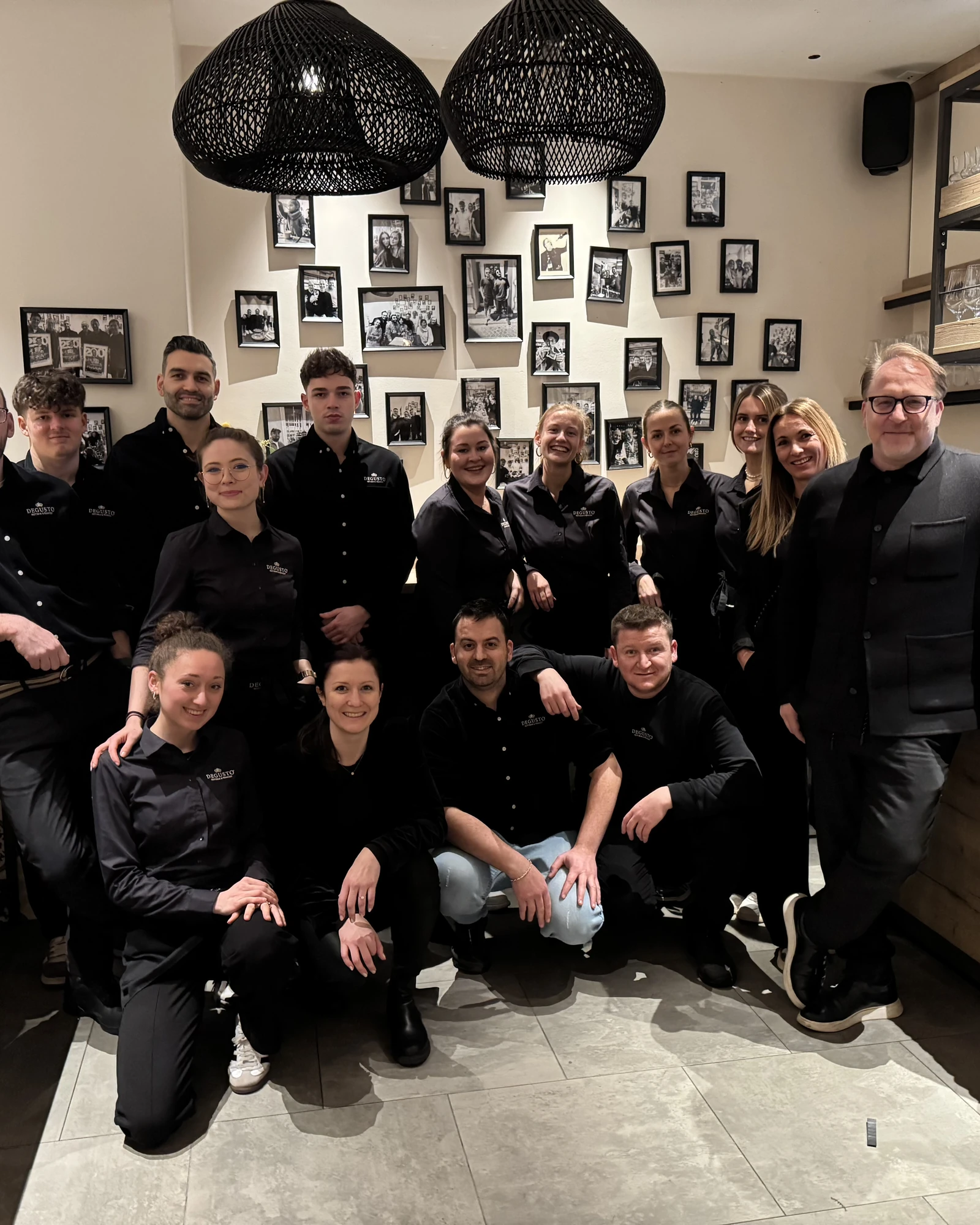 Das DEGUSTO-Team vor der Fotowand im Gastraum, vierzehn Personen